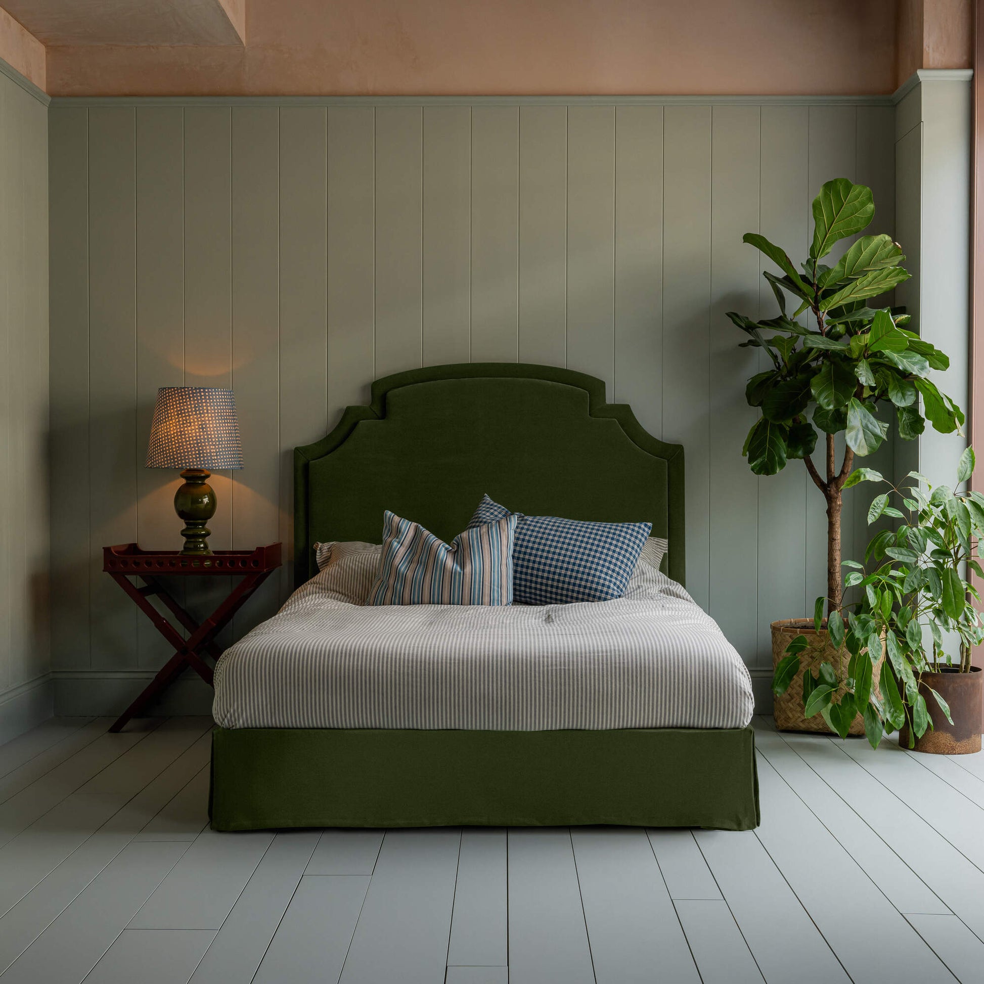 Seventh Heaven Upholstered Bed in Intelligent Velvet Juniper with Kick Pleat Valance, accompanied by a side table lamp, pillows, and a blanket.