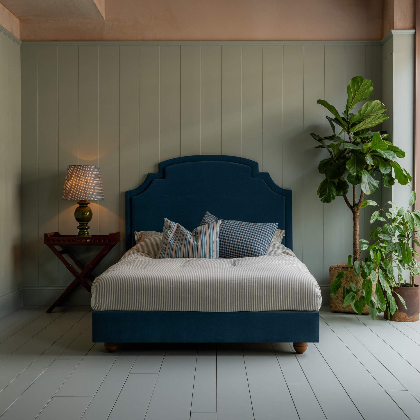 Upholstered bed in laidback linen heather with a ruffled valance, accompanied by a side table with lamp, indoor plant, pillows, and a blanket.