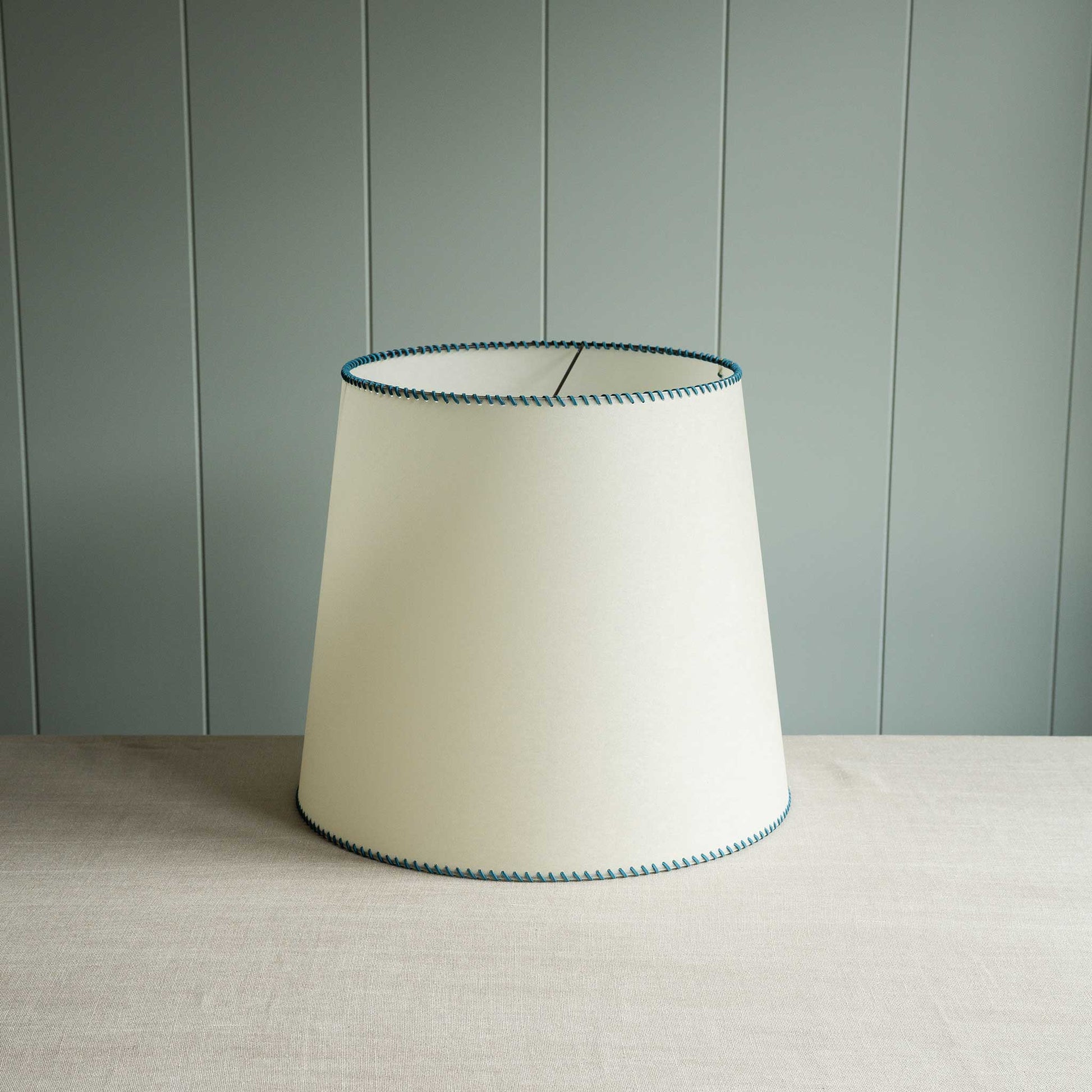 A white lamp shade accented with blue stitching, perfect for contemporary interiors.