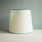 A white lamp shade with blue trim placed on a table, providing soft illumination to the surroundings.