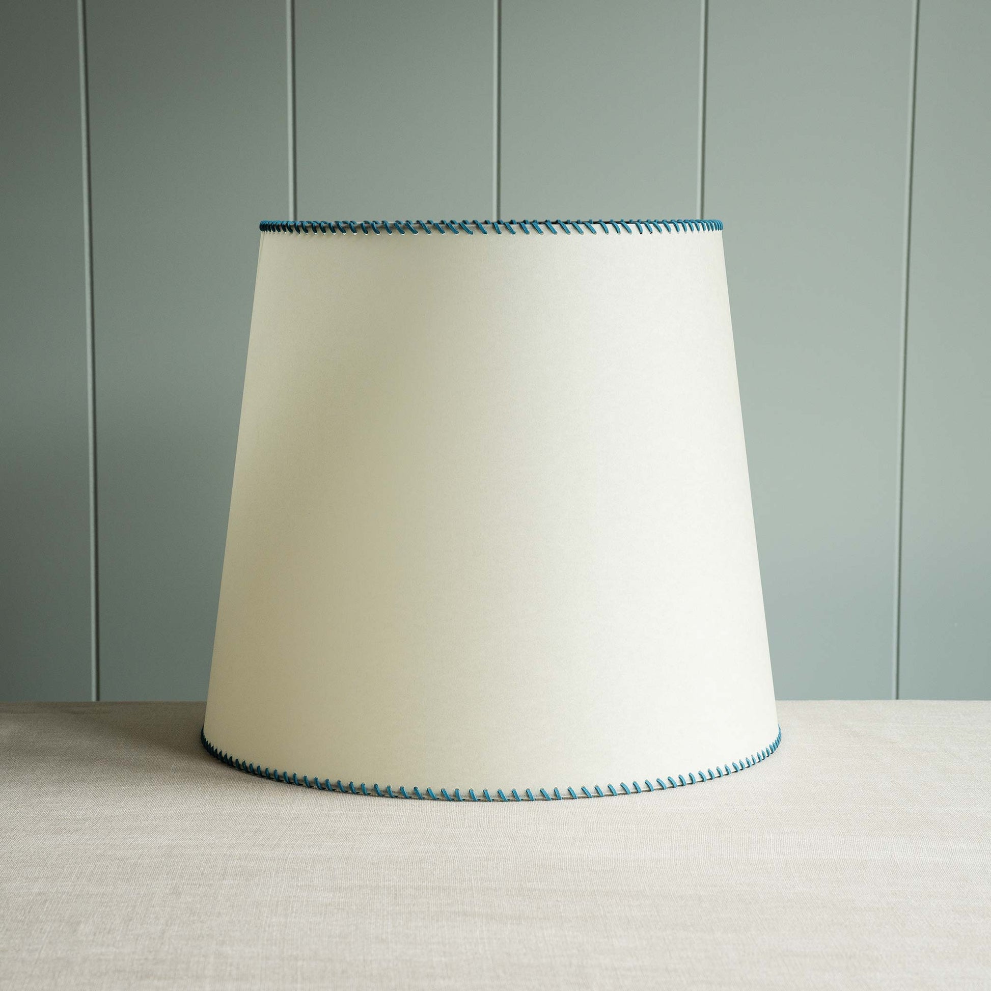 A white lamp shade with blue trim placed on a table, providing soft illumination to the surroundings.