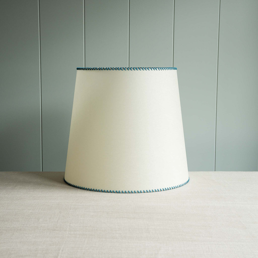  Blue-trimmed white lamp shade displayed on a table. 