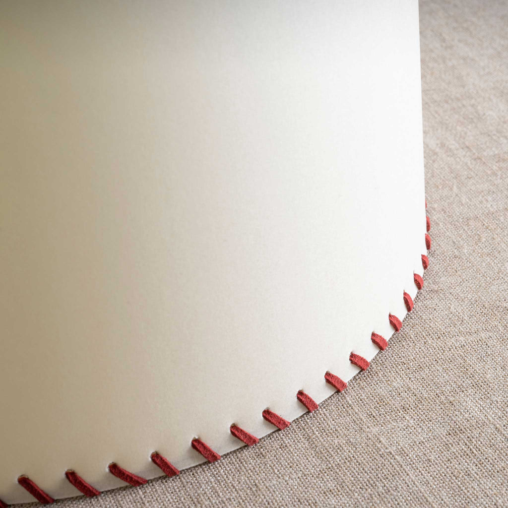  Close-up of sleek white lamp with stylish red stitching detail. 