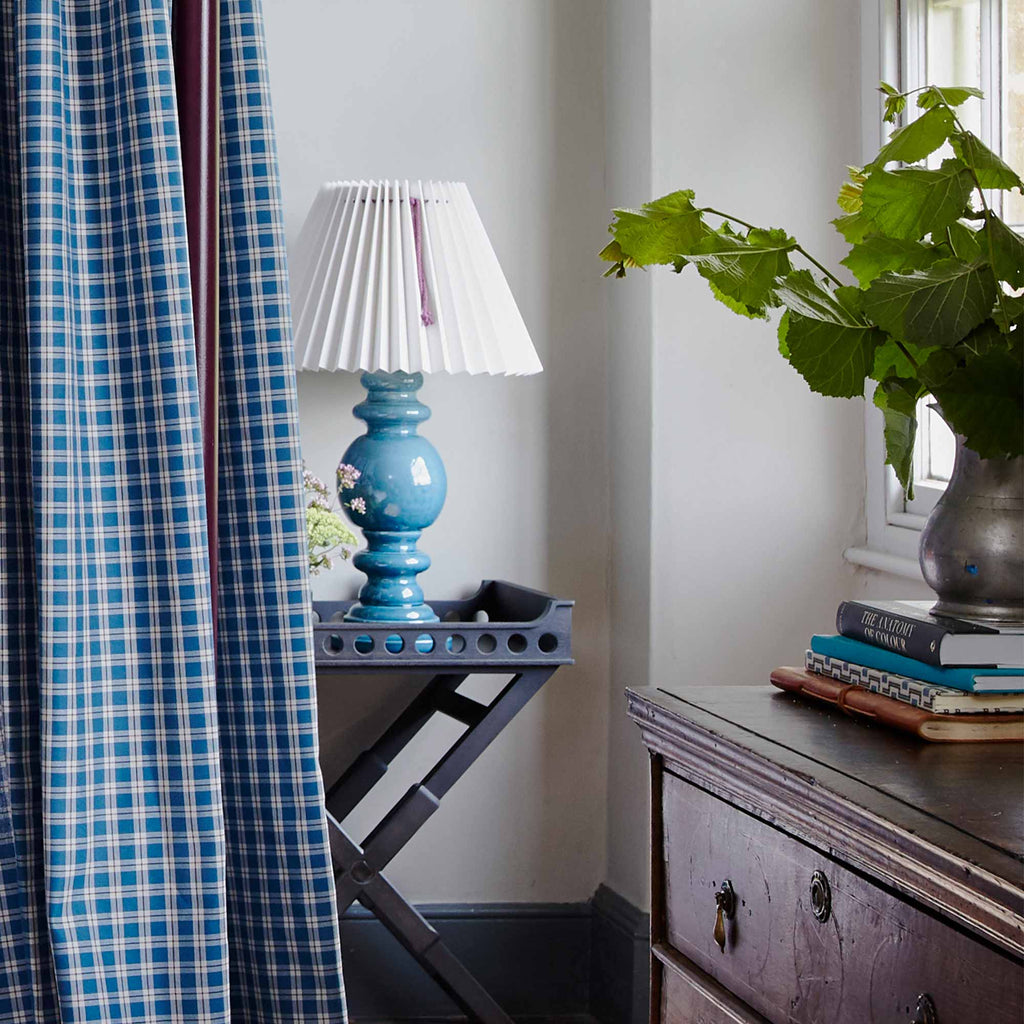  Blue and white checkered curtain hanging in front of lamp. 