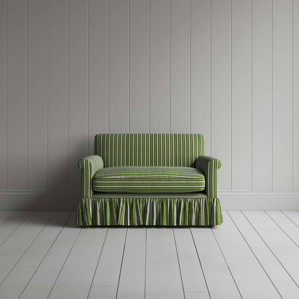  A green couch with a ruffled skirt placed in front of a grey wall. 