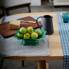  The round dining table is decorated with tea towels, a jug, and a basket of apples, styled by Nicola Harding & Co. 