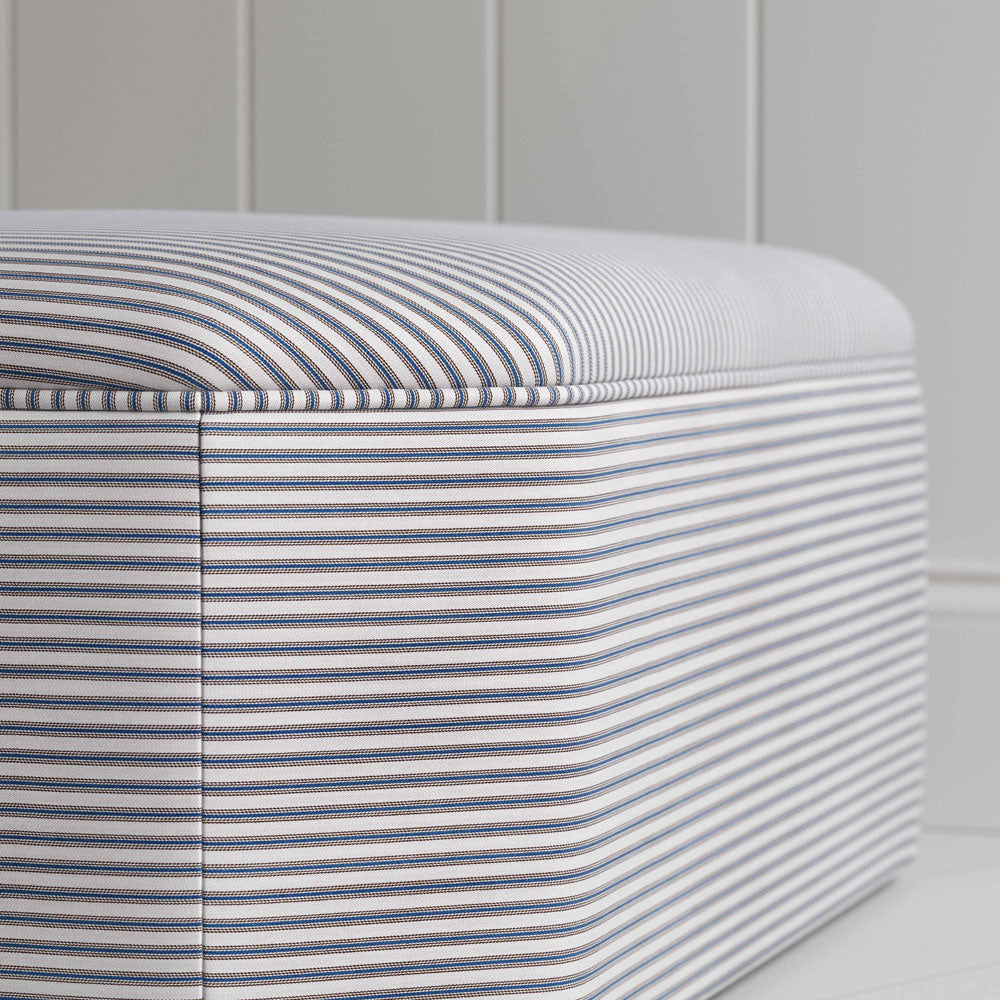  A close up of grey and white striped ottoman on white floor 