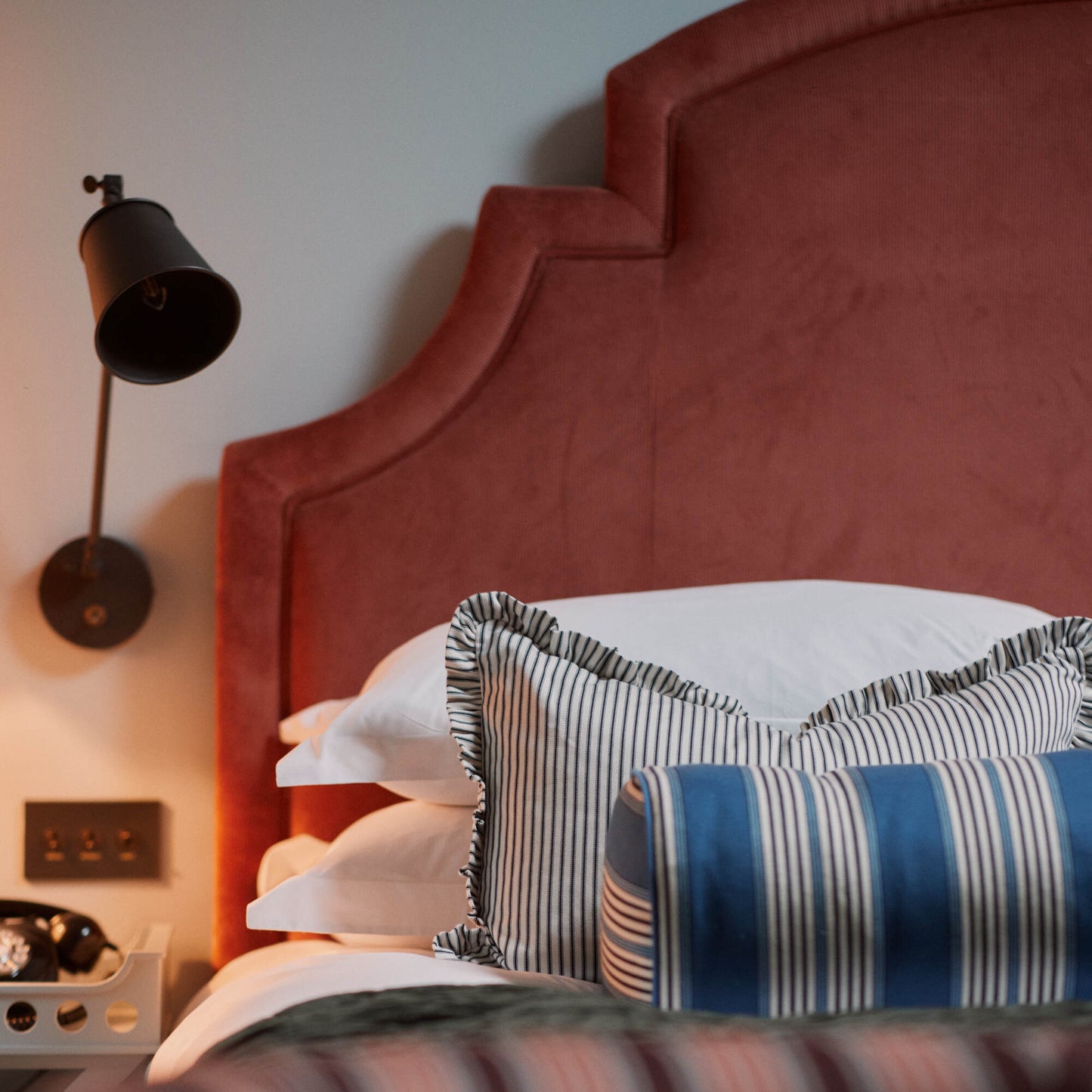 Bed with cushions & pillows and a wall-mounted bedside lamp featuring a waxed brass lampshade Designed By Nicola Harding & Co.