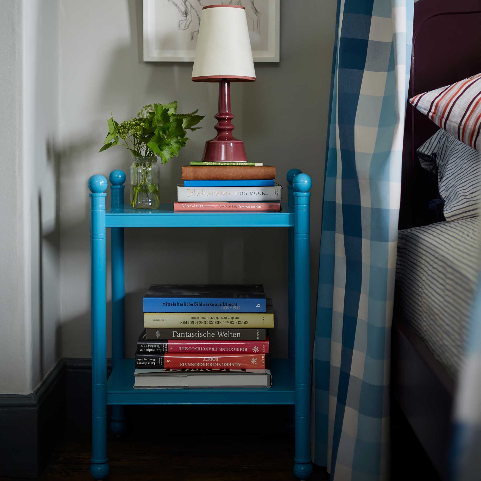  Blue bed side table decorated with books, lamp, and a plant by Nicola Harding & Co. 