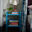  Blue bed side table decorated with books, lamp, and a plant by Nicola Harding & Co. 