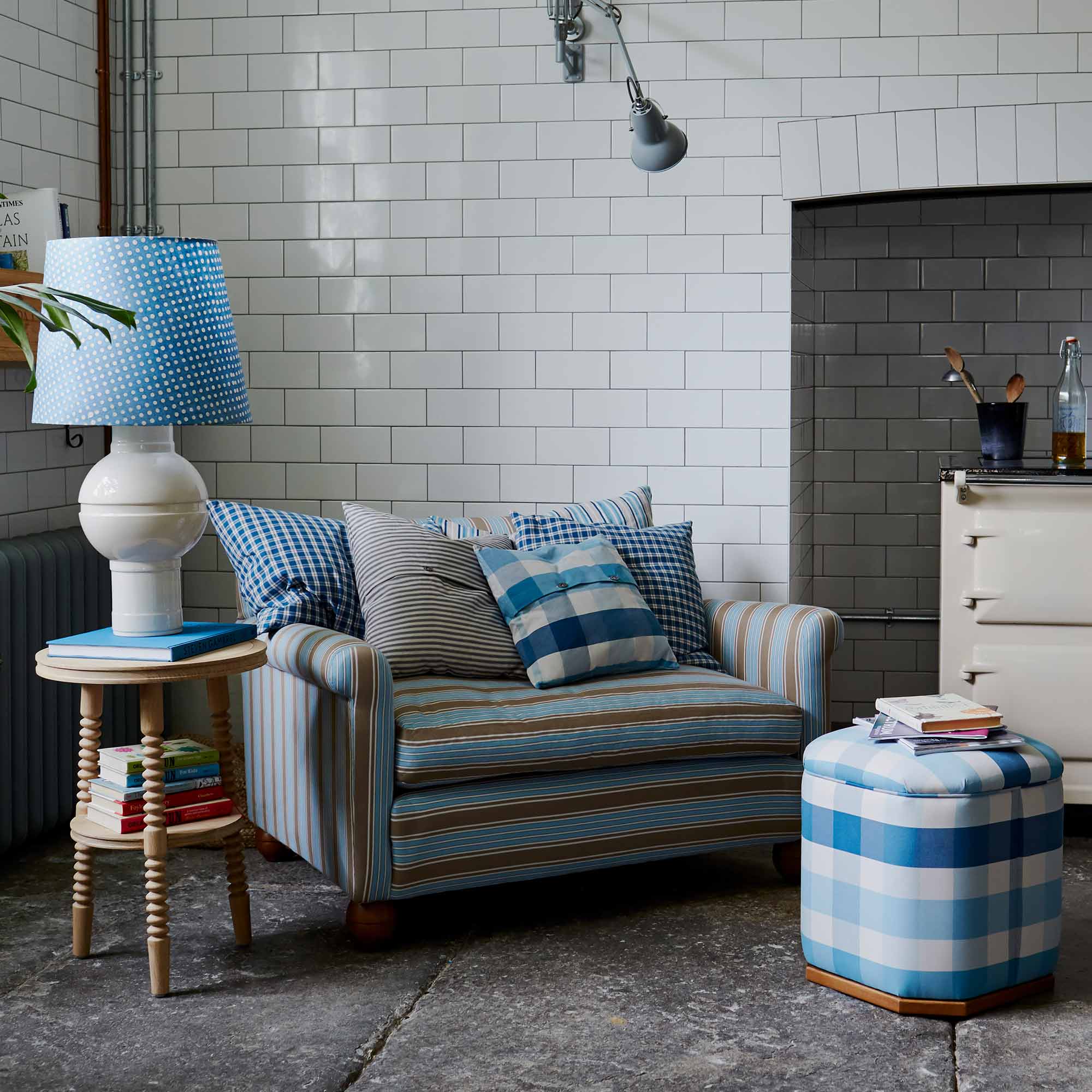  Organized loveseat with cushions next to an ottoman and side table with a white base lamp by Nicola Harding & Co. 