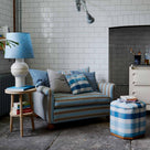  Organized loveseat with cushions next to an ottoman and side table with a white base lamp by Nicola Harding & Co. 