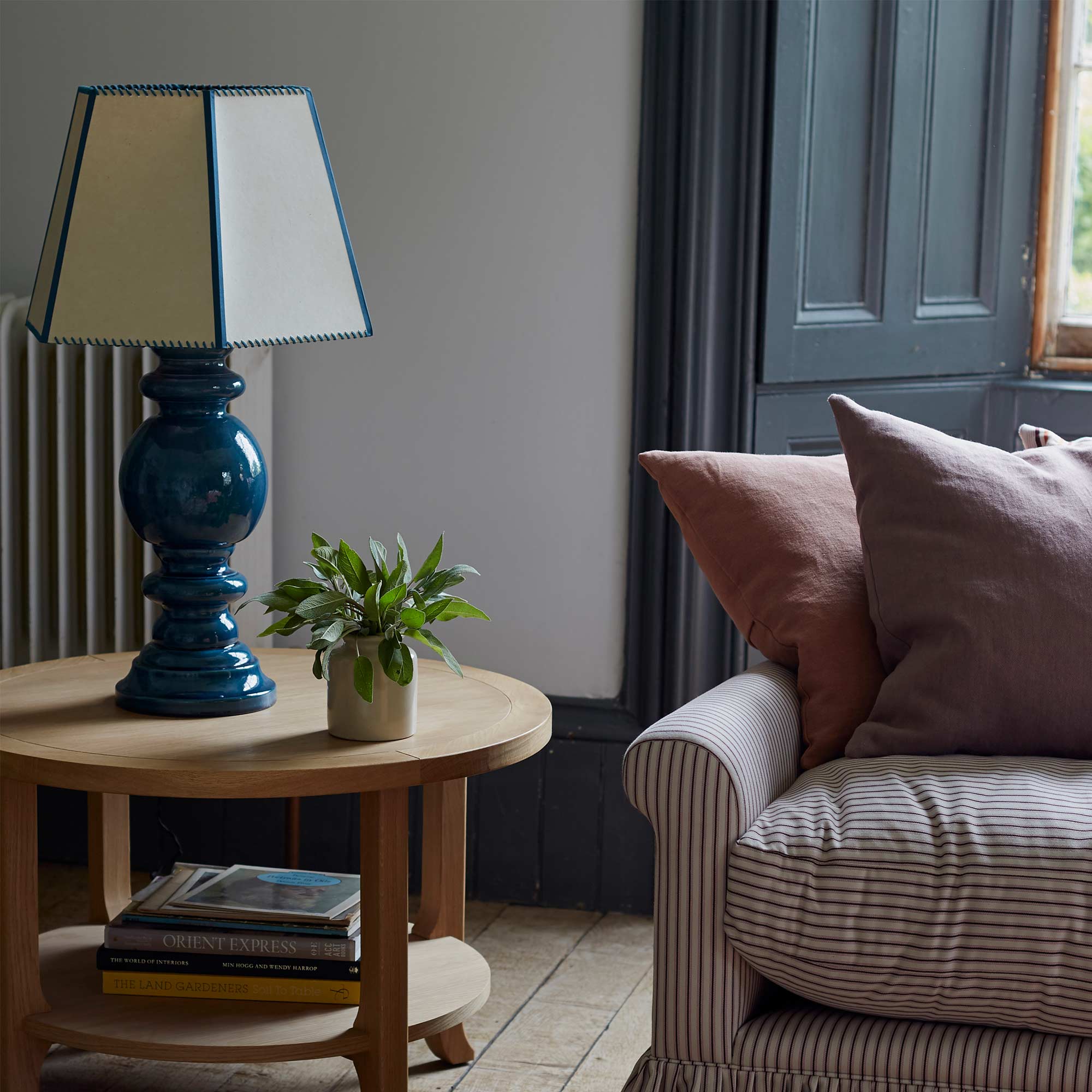  Hourglass Ceramic Table Lamp with Townhouse Hexagonal Lampshade in Soft White with Peacock Blue Trim, on Perk Coffee Table in Oiled Oak, Next to NiX Cotton Tickling Sofa with Cushions – Nicola Harding 