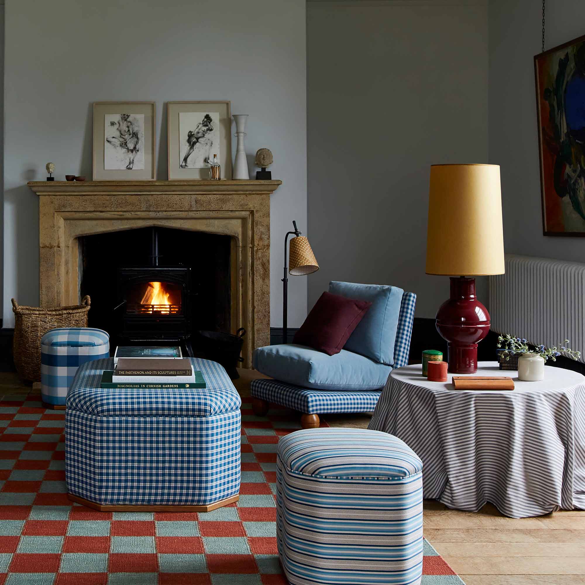  Orb Ceramic Table Lamp Base in Red, With Whimsical Tall Straight Empire Lamp Shade in Mustard with Antiqued Gold Trim, on a Side Table in the Living Room, With a Slipper Chair, 3 Ottomans Near a Fire Place - Nicola Harding 