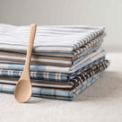  Multiple tea towels displayed with a wooden spoon, styled by Nicola Harding. 