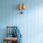 Double Trouble Waxed Brass Wall Light With Mustard Lamp Shades, With Light Blue Wall and a Chair With a Wool Blanket On-it - Nicola Harding 