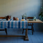  Tuck In rectangular dining table in oak, decorated with cotton fabric, set ready to serve tea with a teapot, cups, and pie, designed by Nicola Harding. 